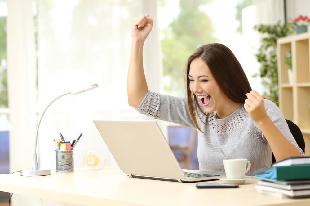 woman celebrating while using laptop